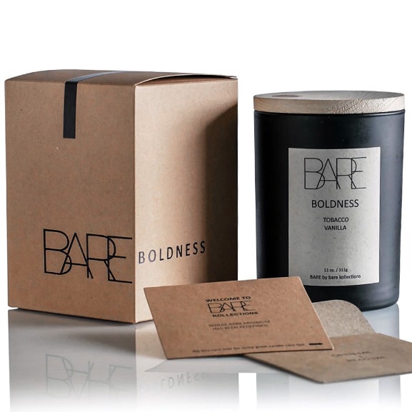 White background. Recycable brown box with Bare logo on the left side. Next to it, on the right side, Boldness, scented candle in a closed black jar with beige label on it.